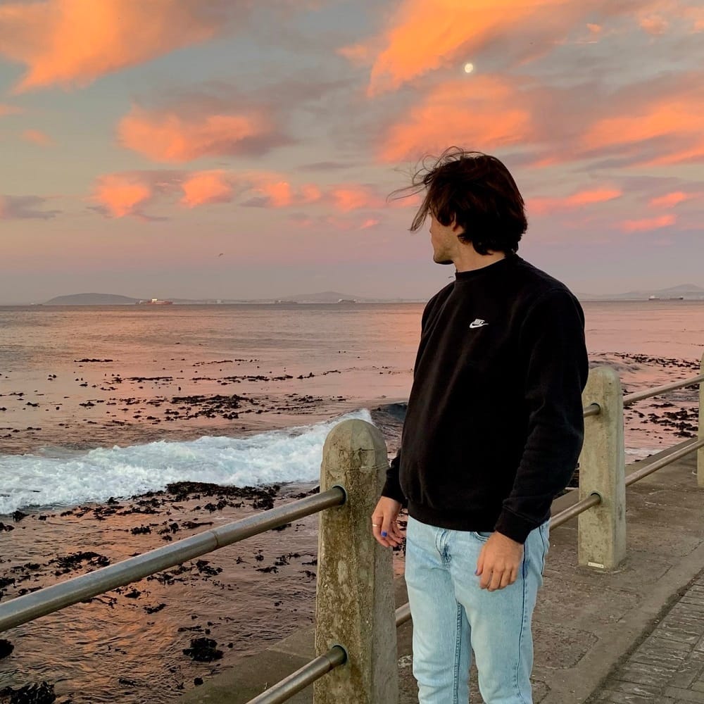 Person standing on a promenade, gazing out at the vast expanse of the ocean.